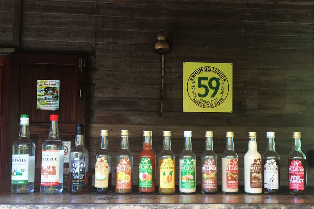 Bouteilles de rhum et de punchs alignées sur un comptoir en bois, sous une plaque « Rhum Bellevue 59° »